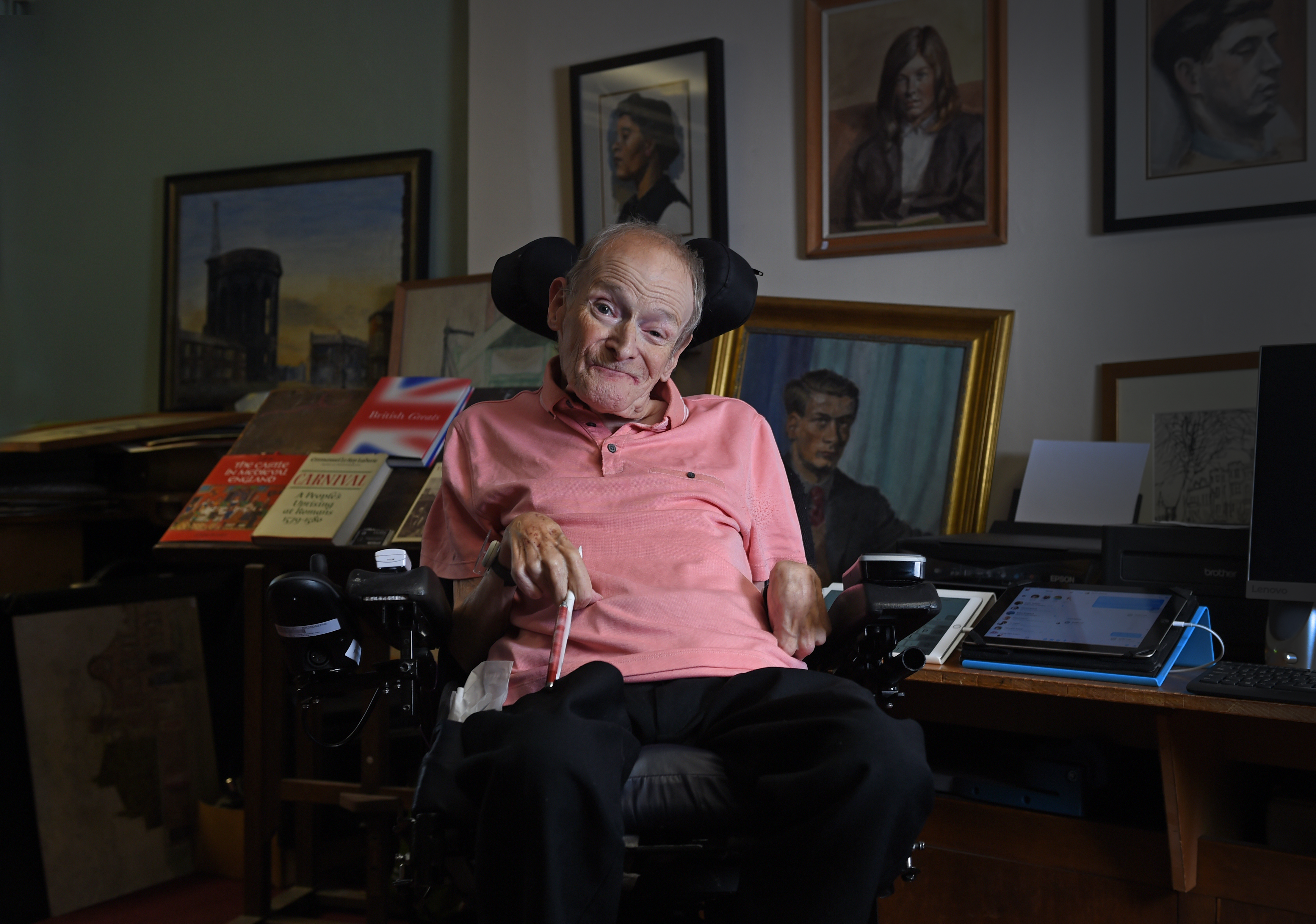 A man in a wheelchair in his house with his paintings in the background