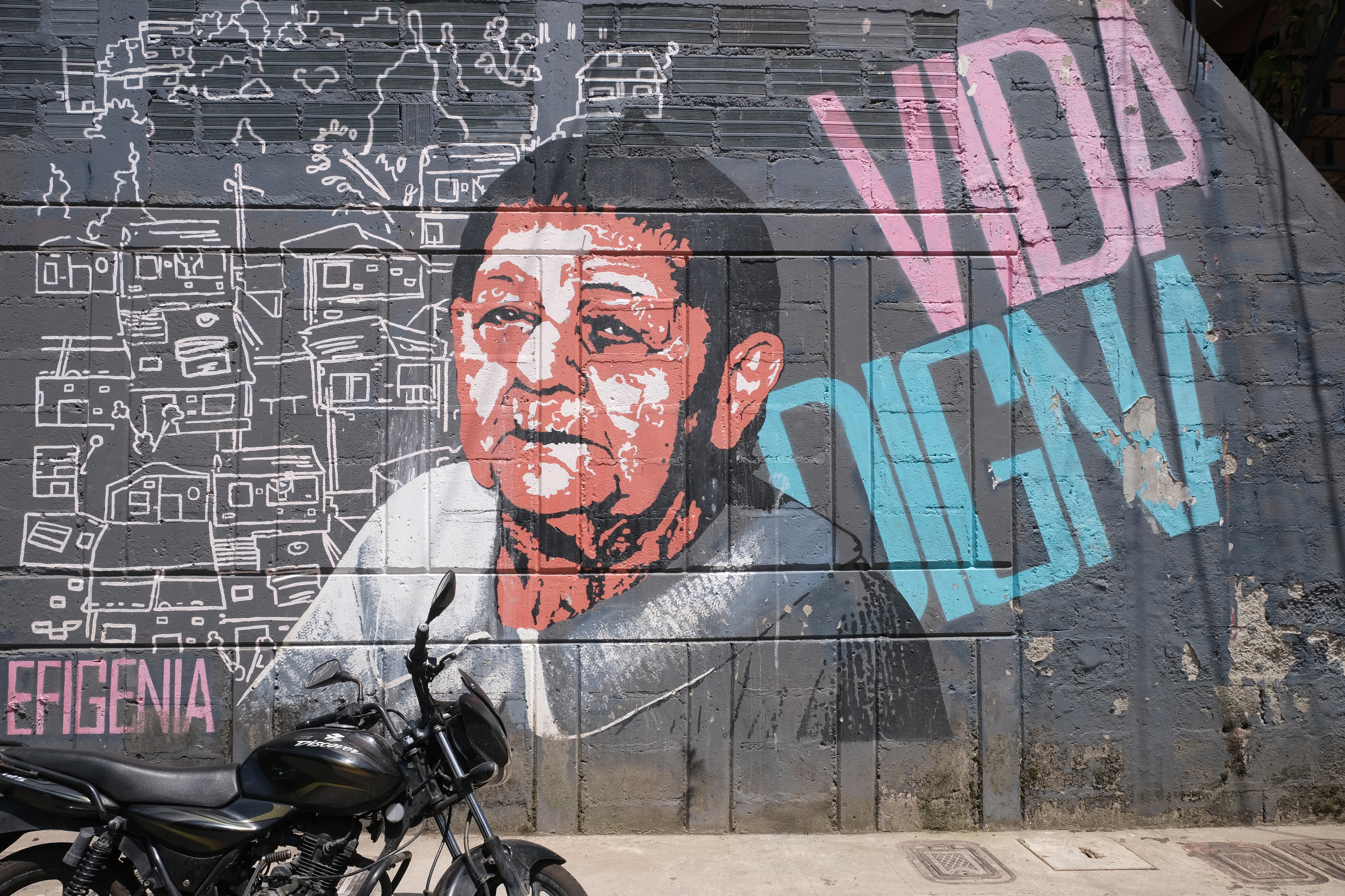 A piture painted on a wall of an older woman with writing saying "Vida Digna" next to her and a motorbike in the foreground